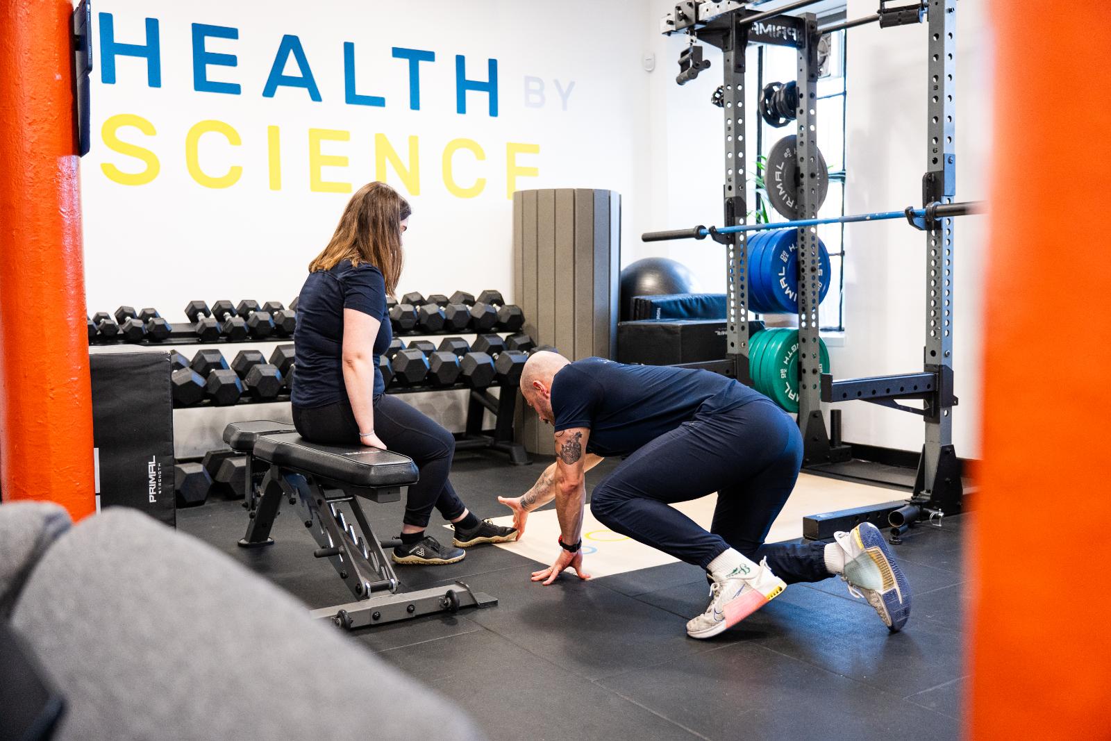 A coach guiding a client through a floor-based mobility and movement assessment at the Leith clinic.