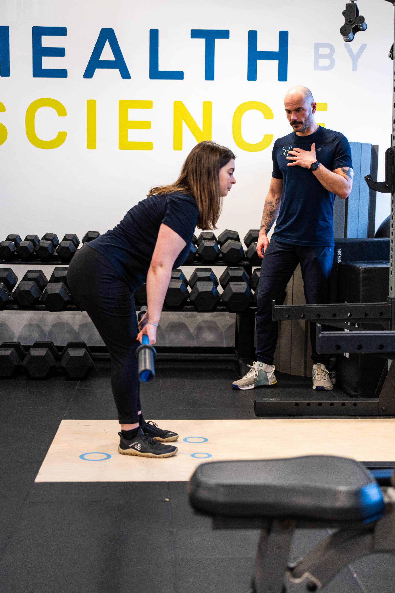 Health by Science specialist providing clinical cues for a barbell Romanian deadlift to assess posterior chain engagement.