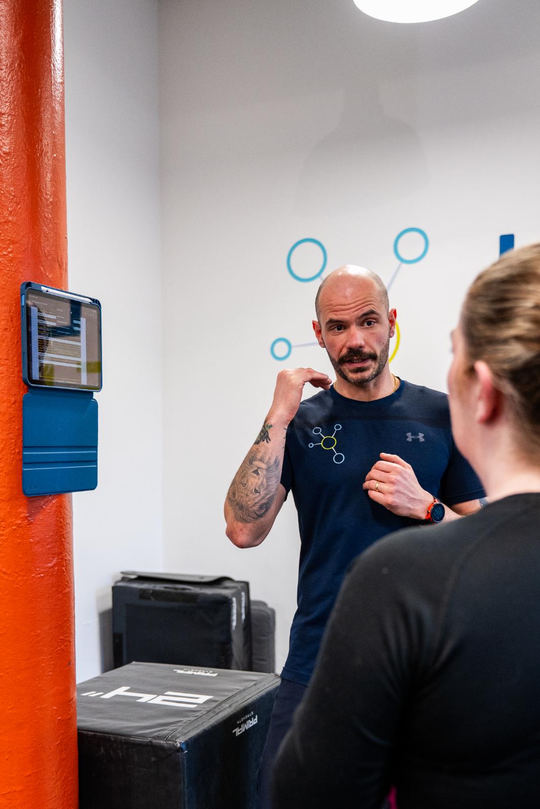 Practitioner explaining movement mechanics and rehabilitation progress using a wall-mounted tablet interface.