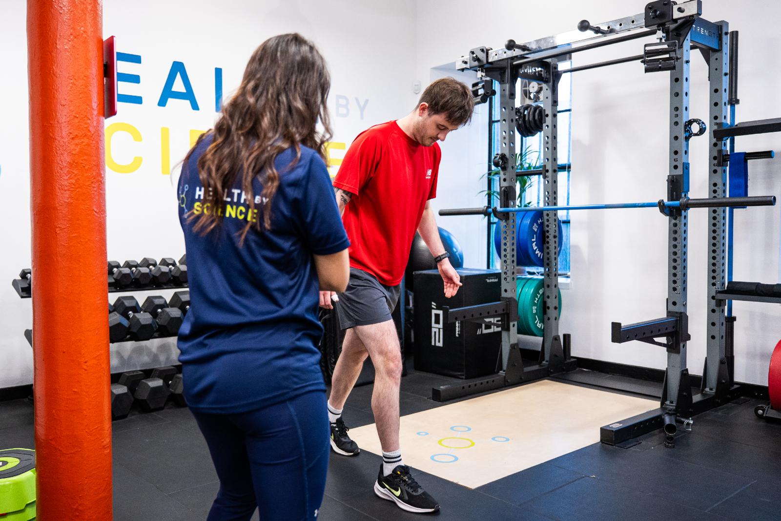 A personal trainer conducting a movement assessment with a male client in a gym setting.