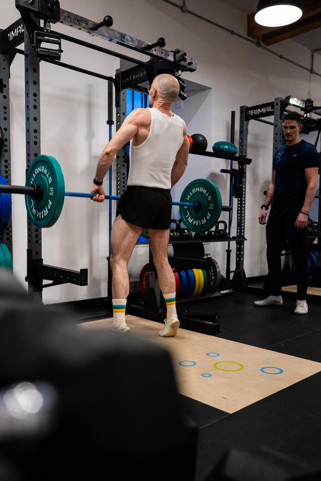 Clinical supervision of a barbell clean and press to assess upper body explosive power and overhead stability.