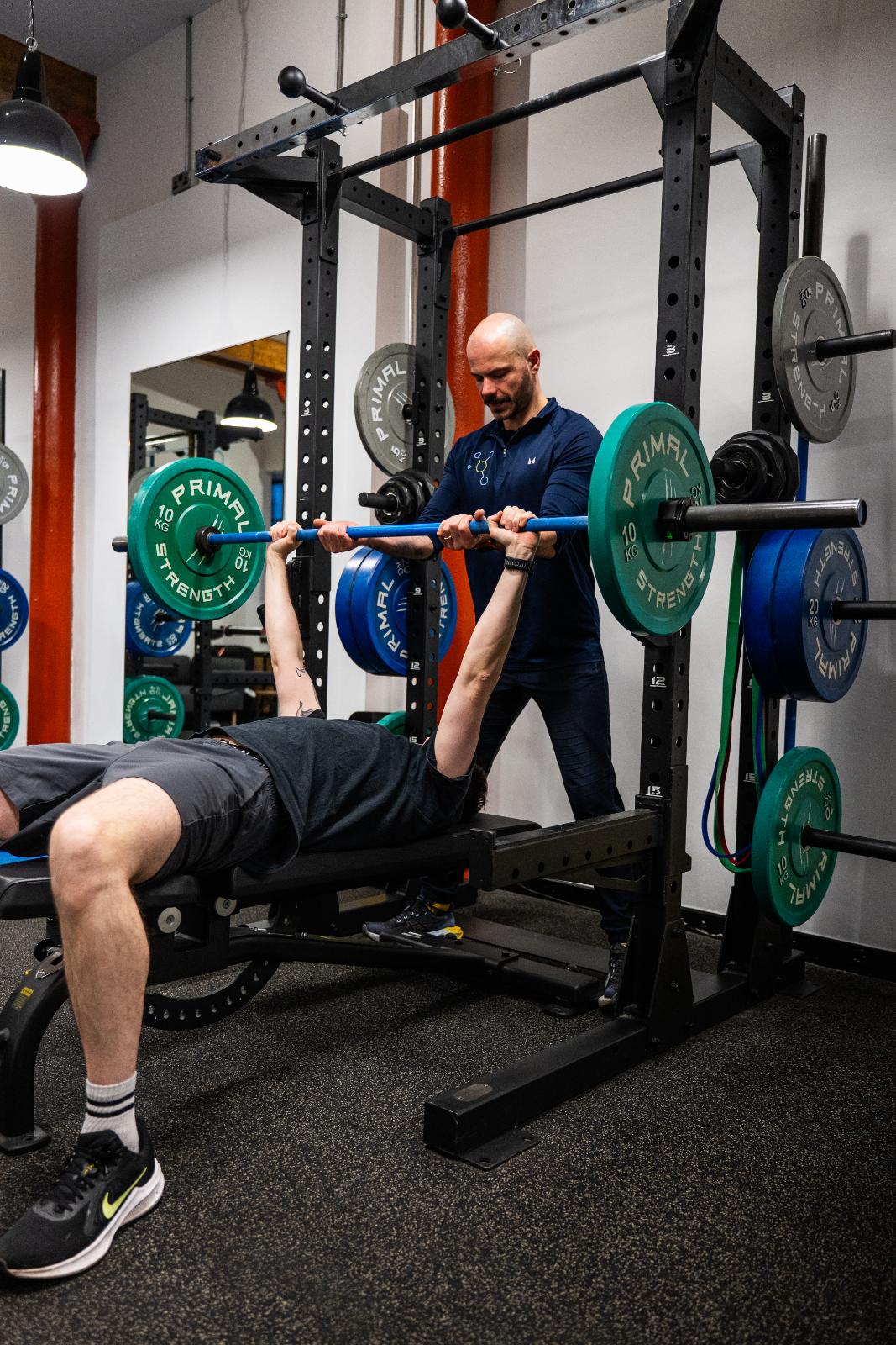 Senior coach providing a safe spot and technical feedback for a barbell bench press during a personal training Edinburgh session.