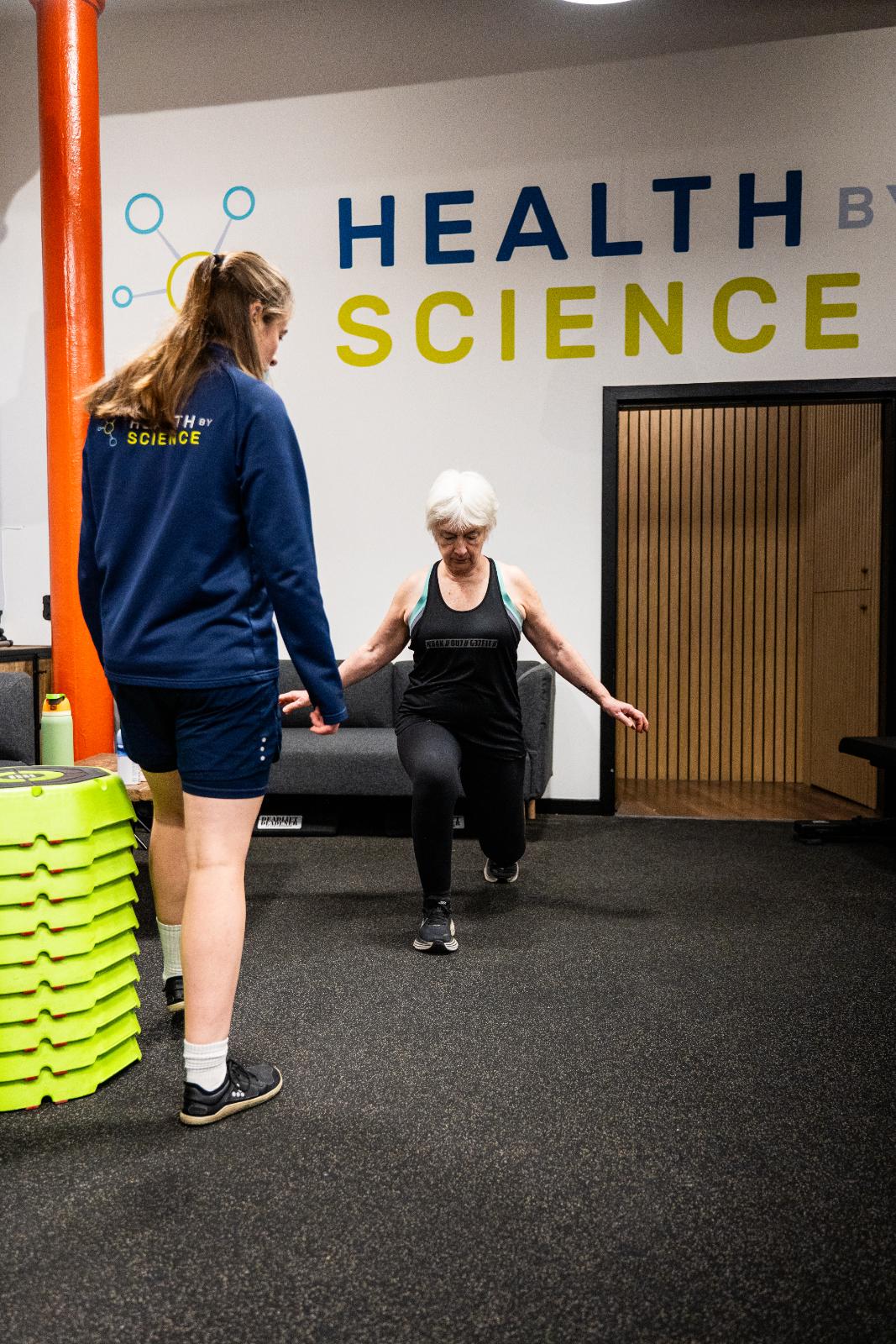 Specialist observing a senior patient’s lunging mechanics to ensure safe joint alignment during a personal training session.