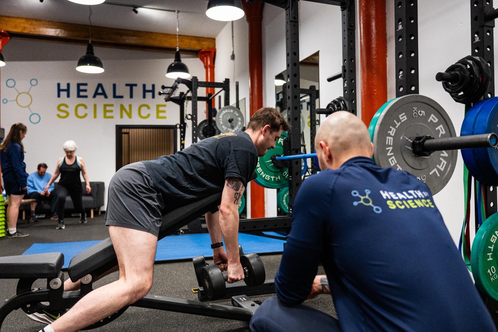 Health by Science coach monitoring lifting mechanics during a strength-based rehabilitation session at our Leith clinic.