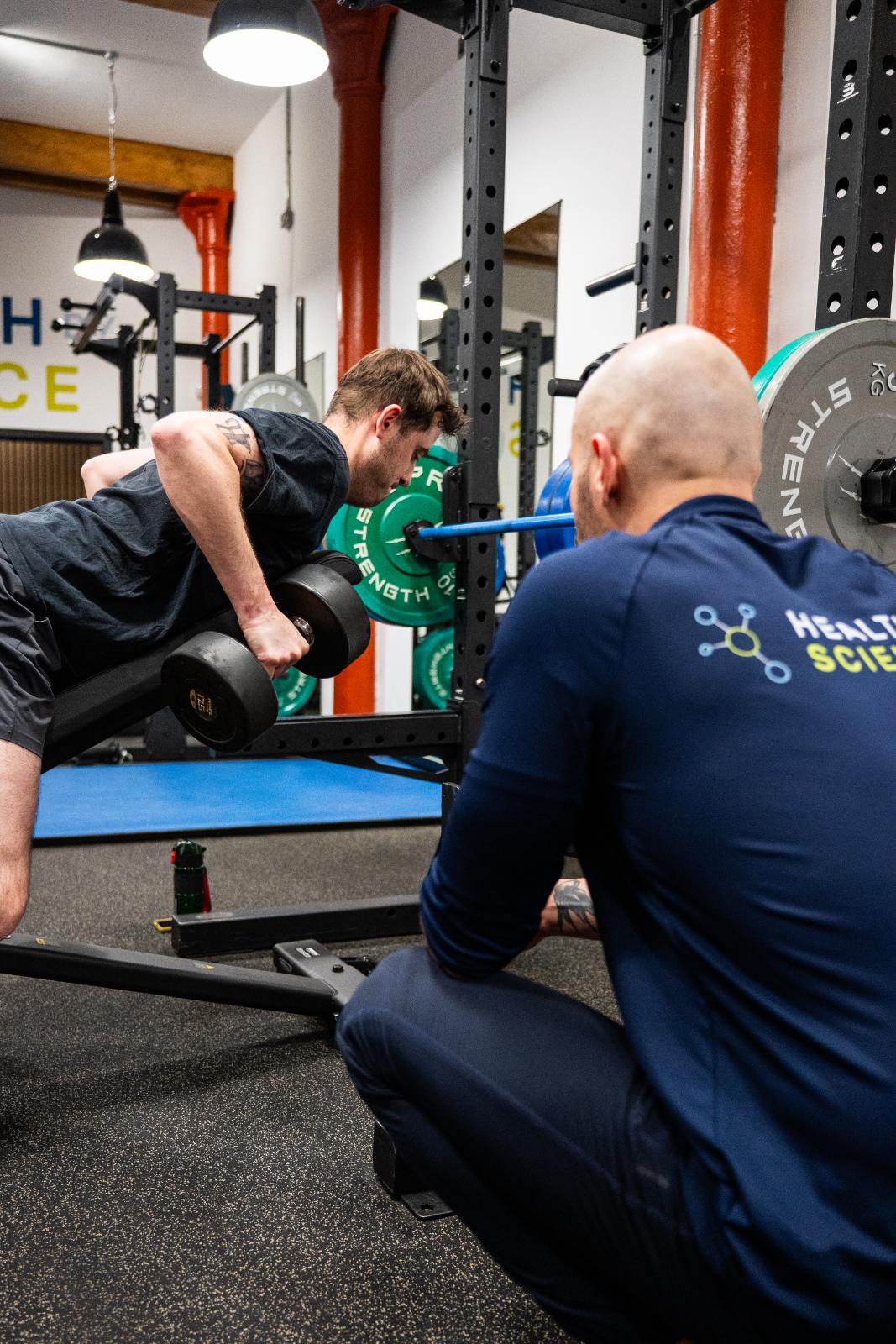 Specialist providing clinical movement instruction for a chest-supported dumbbell row to improve postural health.