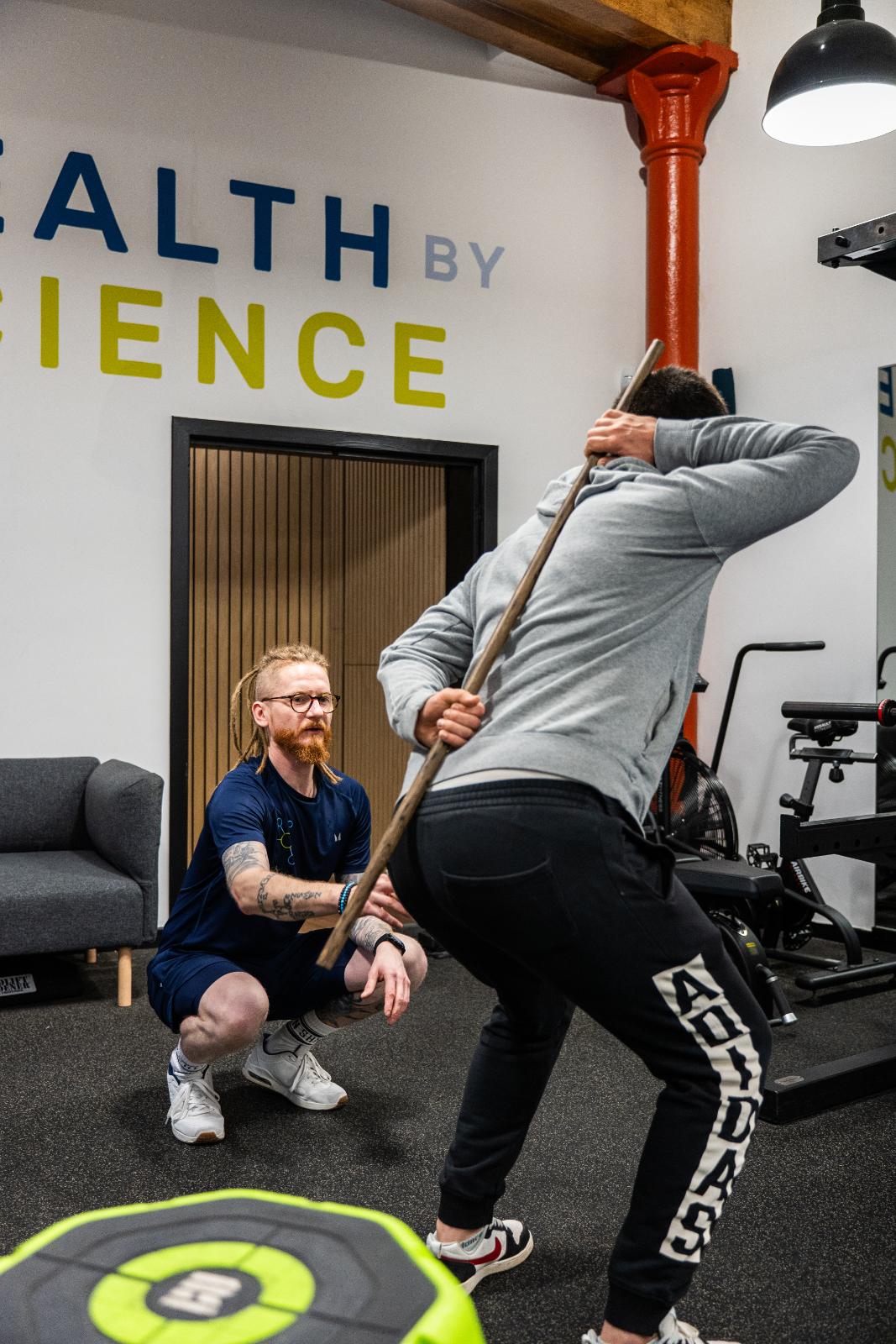 Specialist conducting a biomechanical assessment using a dowel to analyse hip hinge and spinal alignment in our Leith clinic.