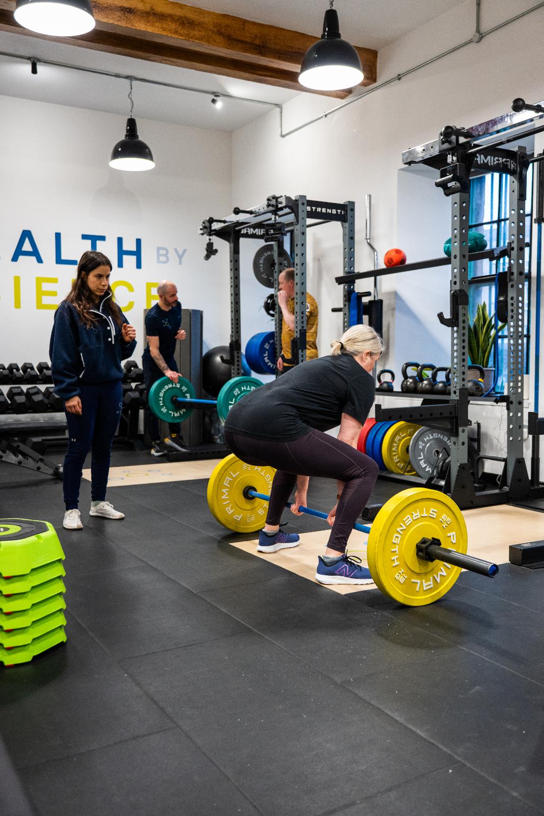 Health by Science coach overseeing a barbell deadlift to ensure safe lumbar mechanics during a clinical personal training session.