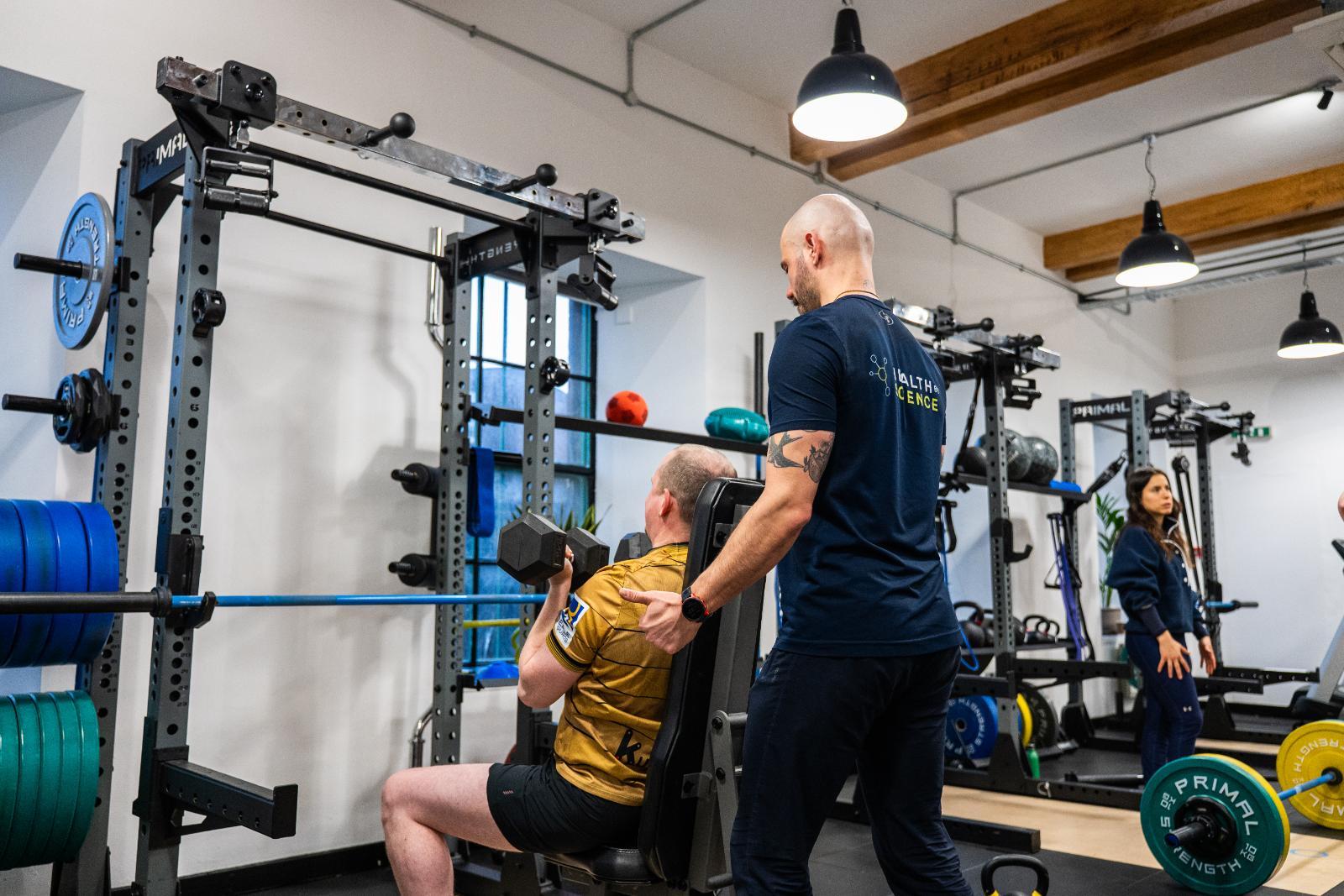 Clinical specialist providing a tactile cue and spotting during a seated dumbbell overhead press for personal training Edinburgh.