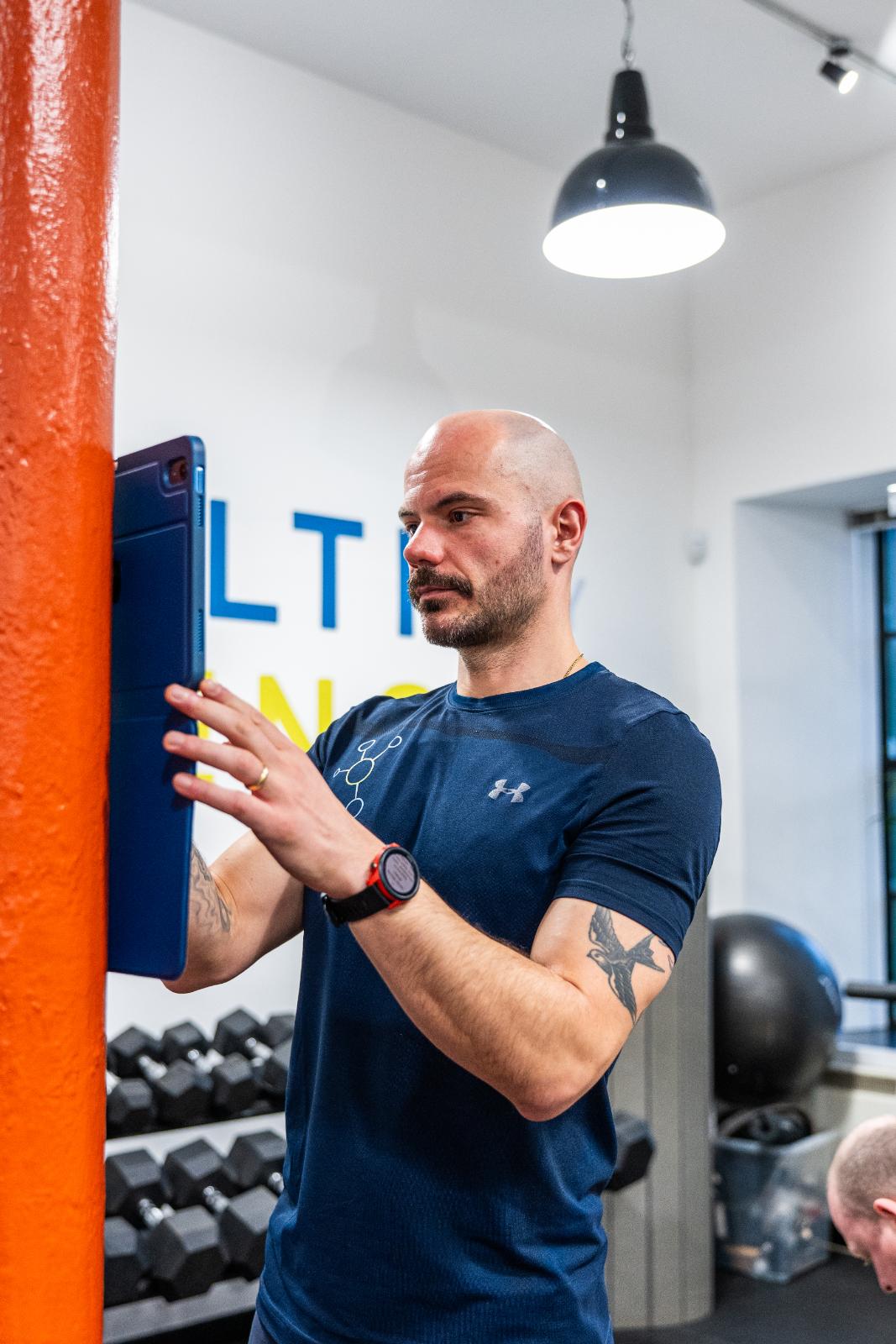 Health by Science practitioner using a digital assessment tool to monitor real-time biometric data during a clinical gym session.