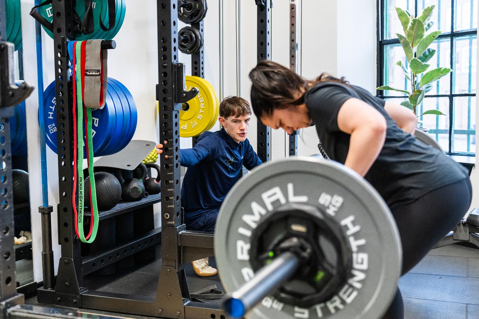 Professional monitoring of a bent-over barbell row to ensure safe spinal alignment during a personal training Edinburgh session.
