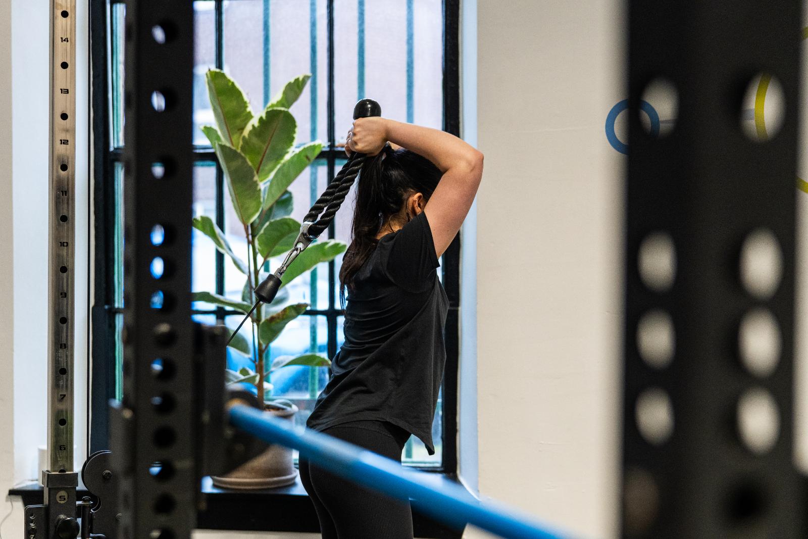 Client performing a cable overhead triceps extension under clinical supervision to improve upper body strength and joint stability.