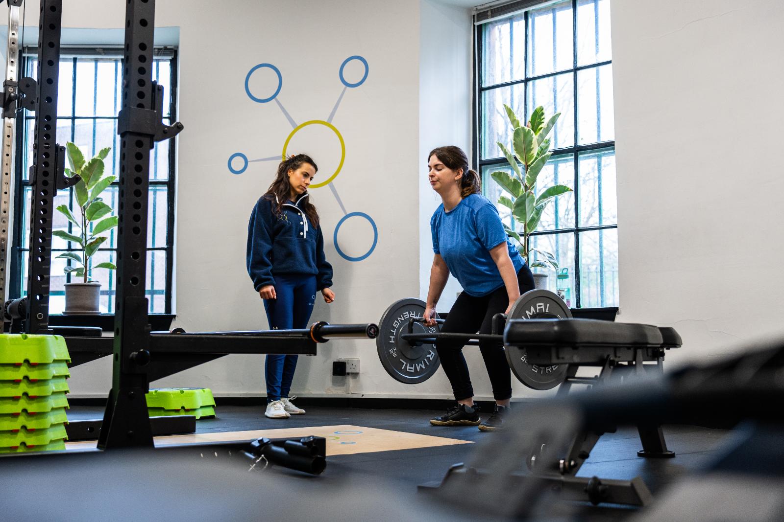 A female personal trainer edinburgh coaching a woman during a barbell deadlift in a bright, modern gym in Leith.