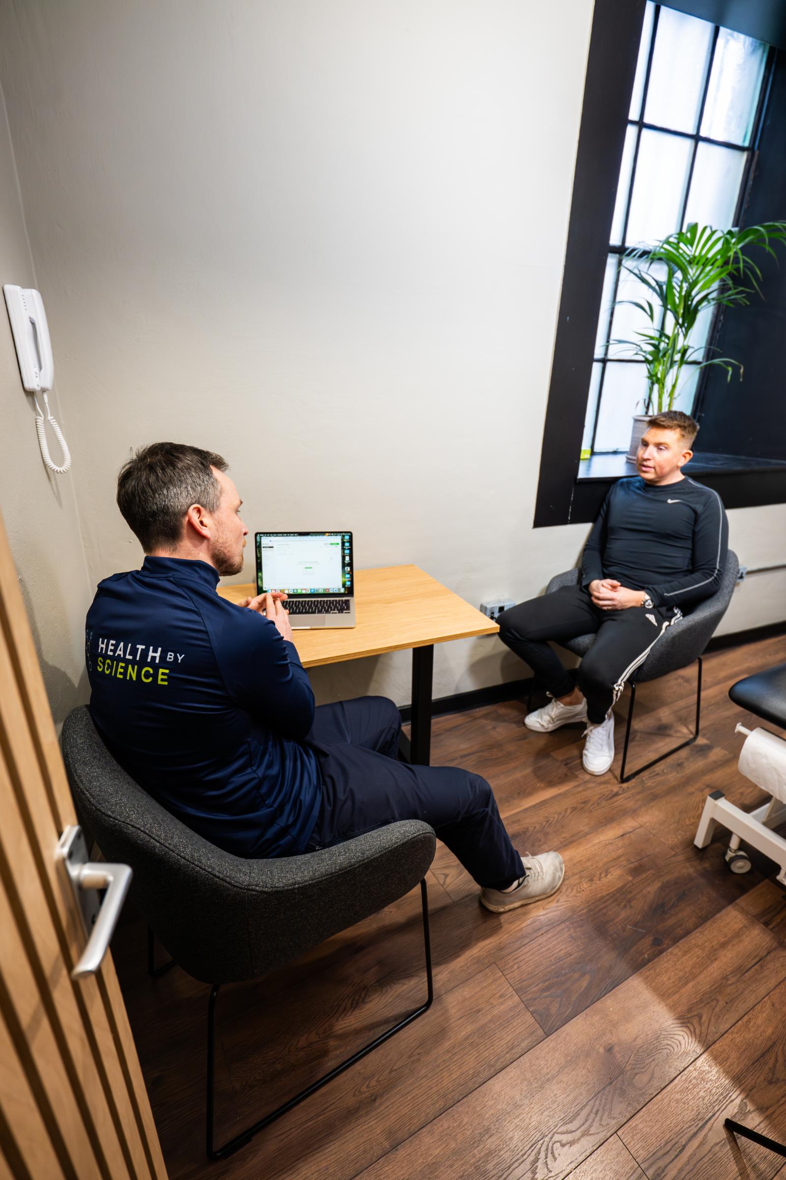 Health by Science specialist using a laptop to track real-time clinical biometrics during a one-to-one patient session.