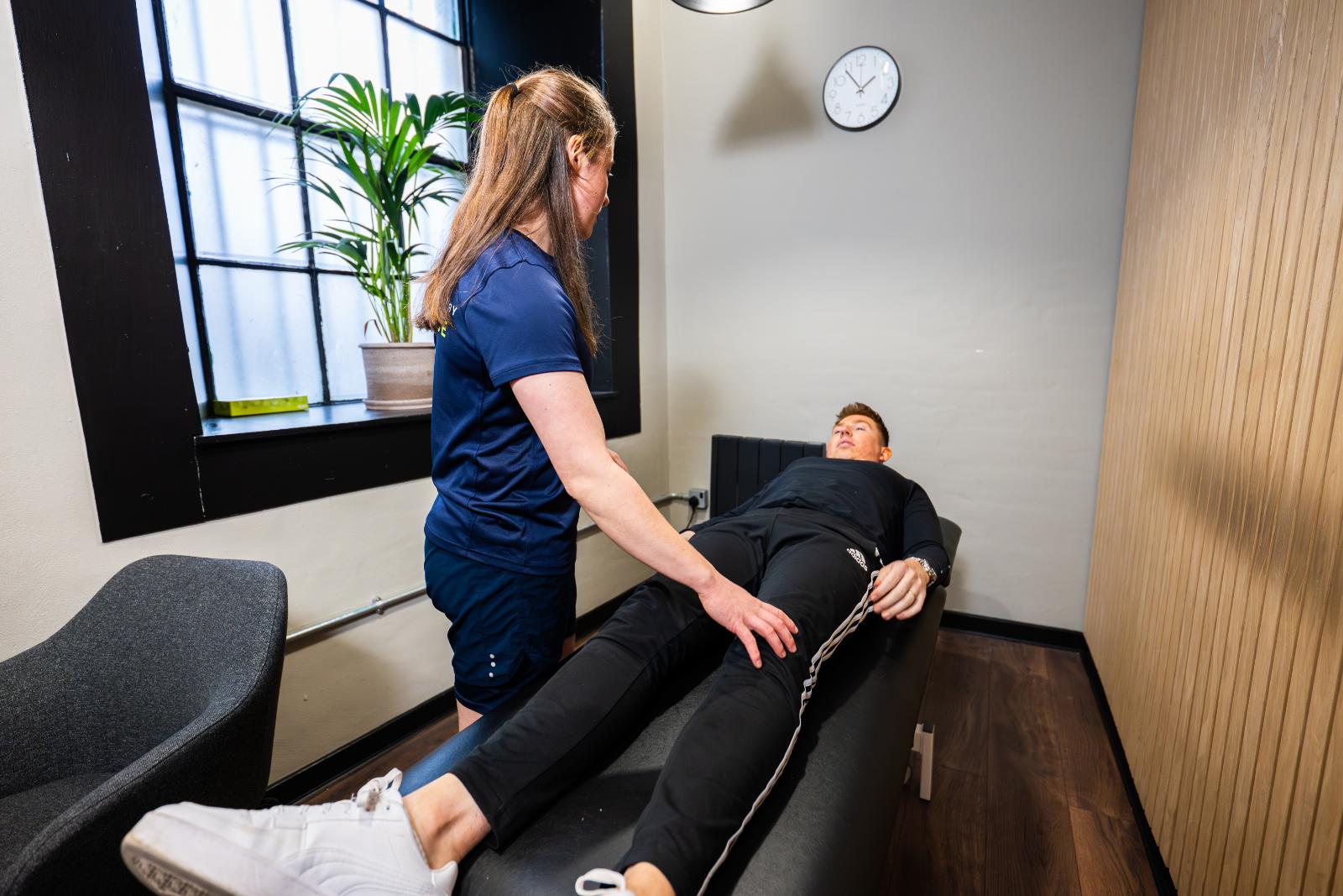 A female physiotherapist performing a manual therapy assessment on a patient's leg on a treatment table.