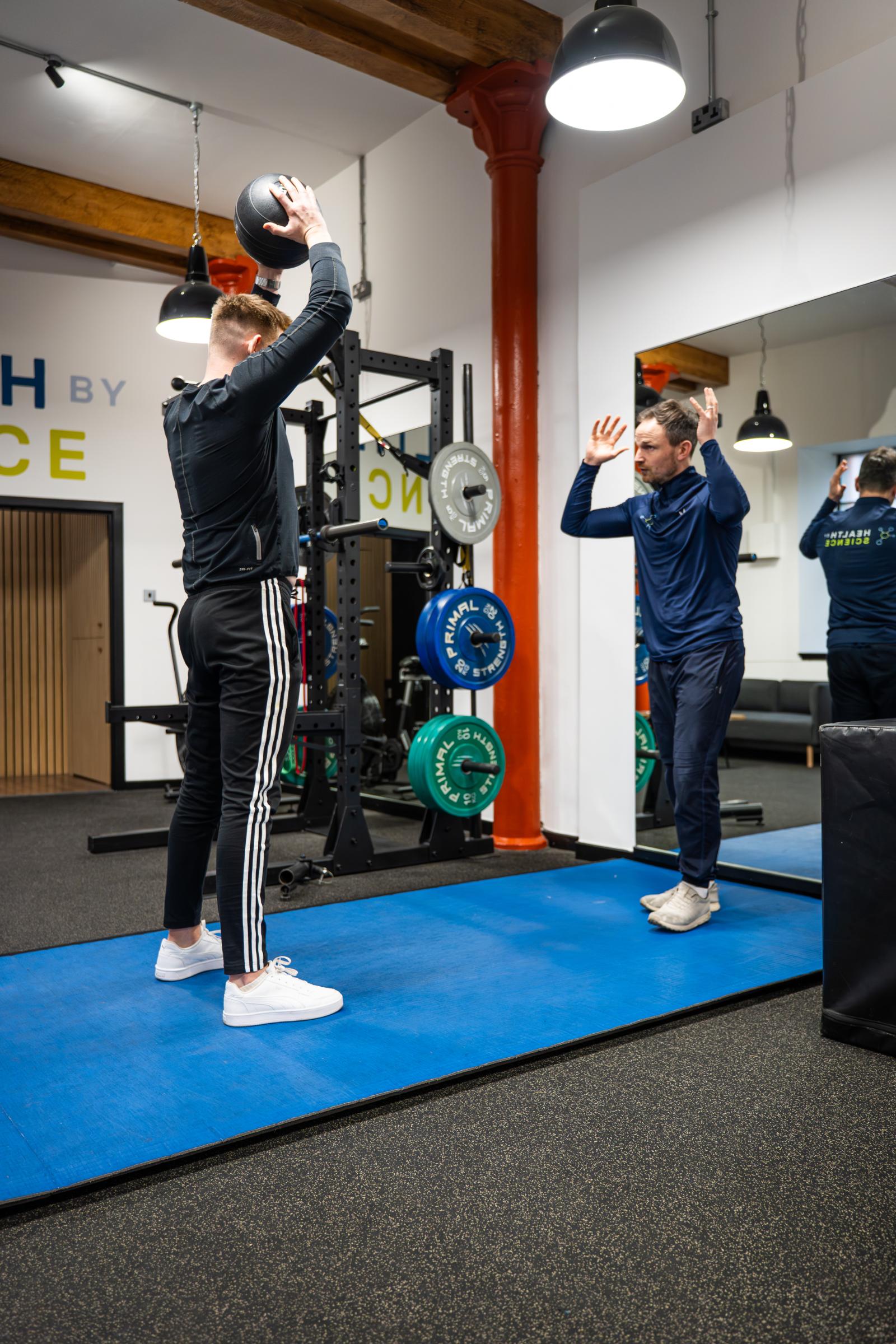Specialist providing technical feedback on overhead medicine ball positioning to ensure optimal shoulder mechanics and core engagement.