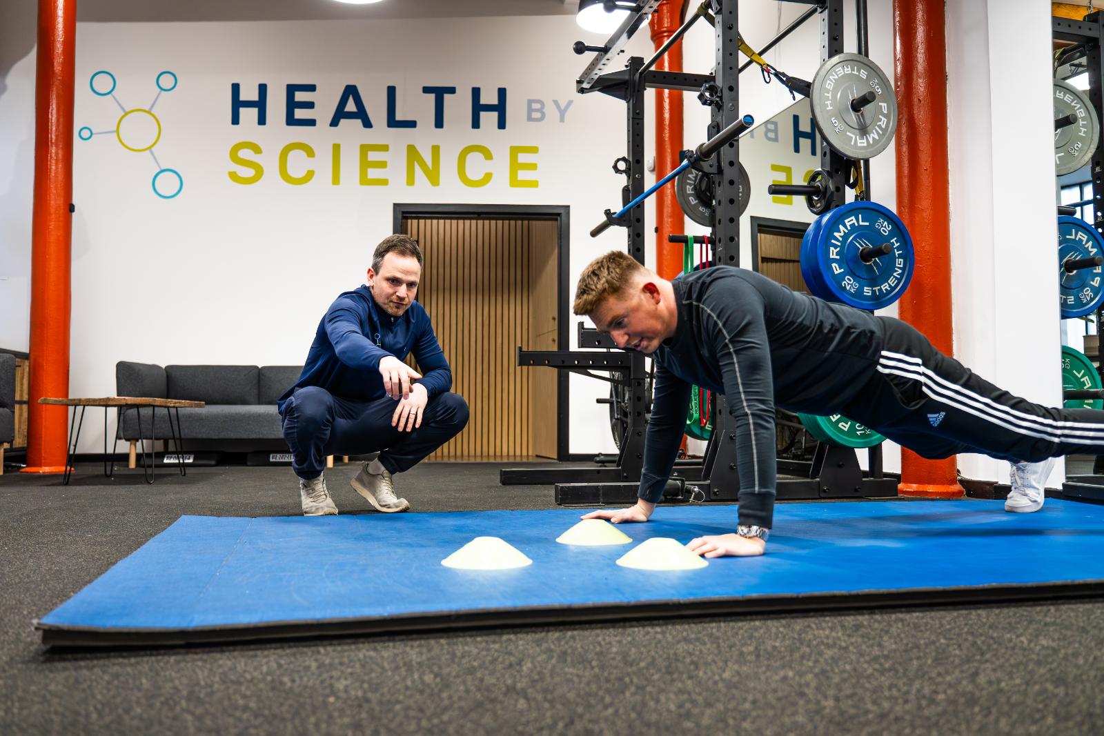 A physiotherapist in edinburgh coaching a man through a floor-based rehabilitation exercise using cones for positioning.