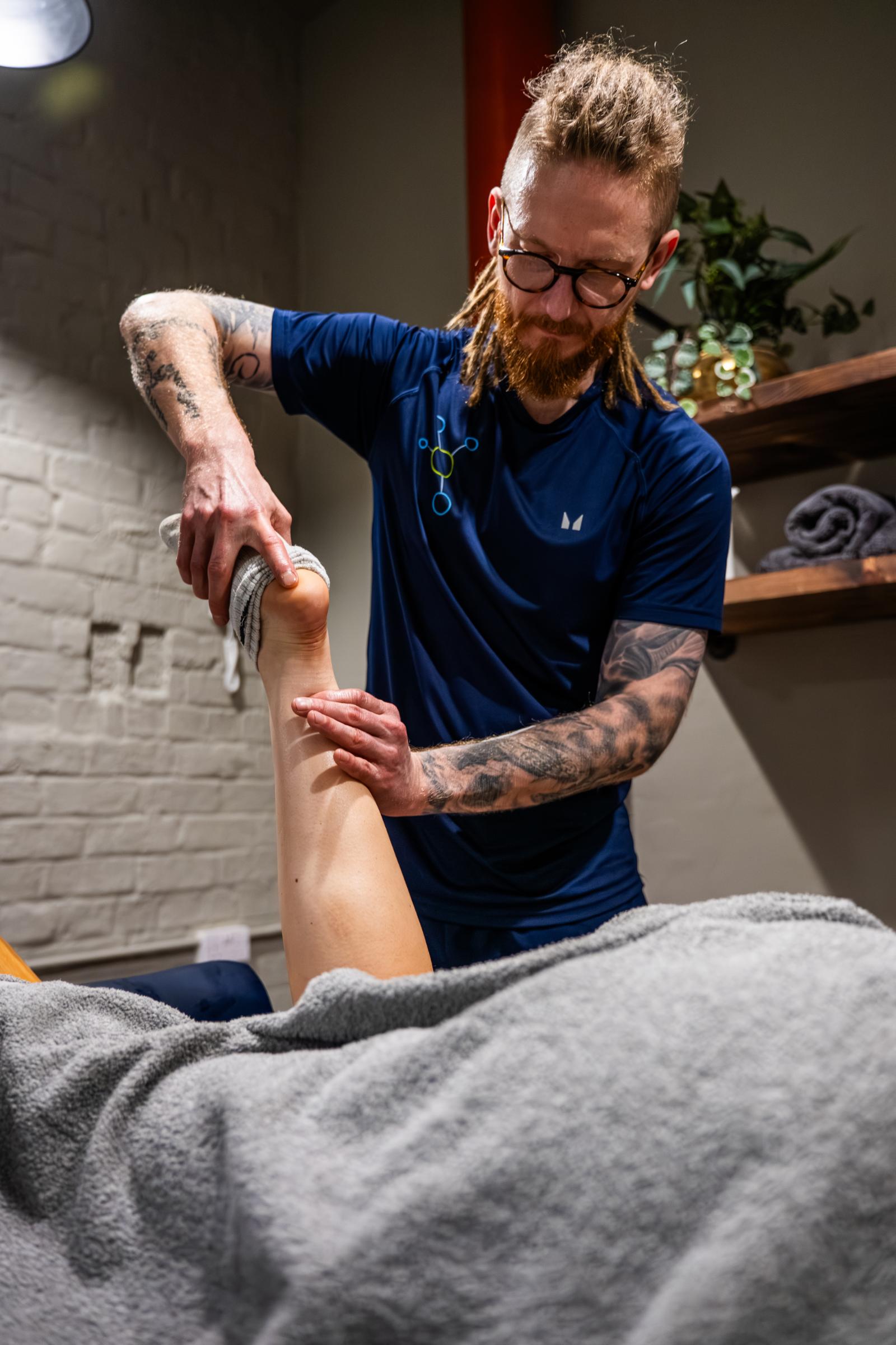 Health by Science specialist conducting a clinical manual assessment of ankle joint range of motion on a treatment plinth.